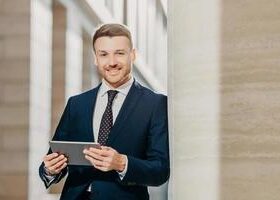 confident-cheerful-male-lawyer-reads-business-news-has-gentle-smile-dressed-in-formal-clothes-poses-in-urban-setting-businessman-checks-email-or-updates-profile-on-digital-tablet-computer-photo